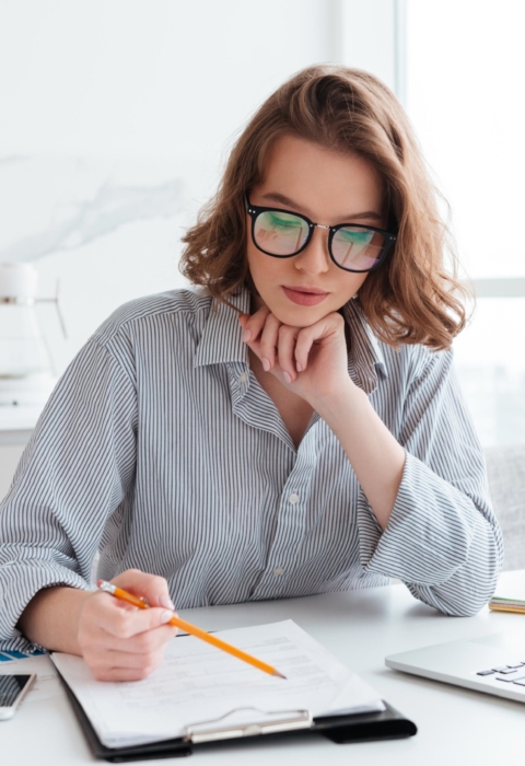 young-concentrated-businesswoman-in-glasses-and-striped-shirt-working-with-papers-at-home